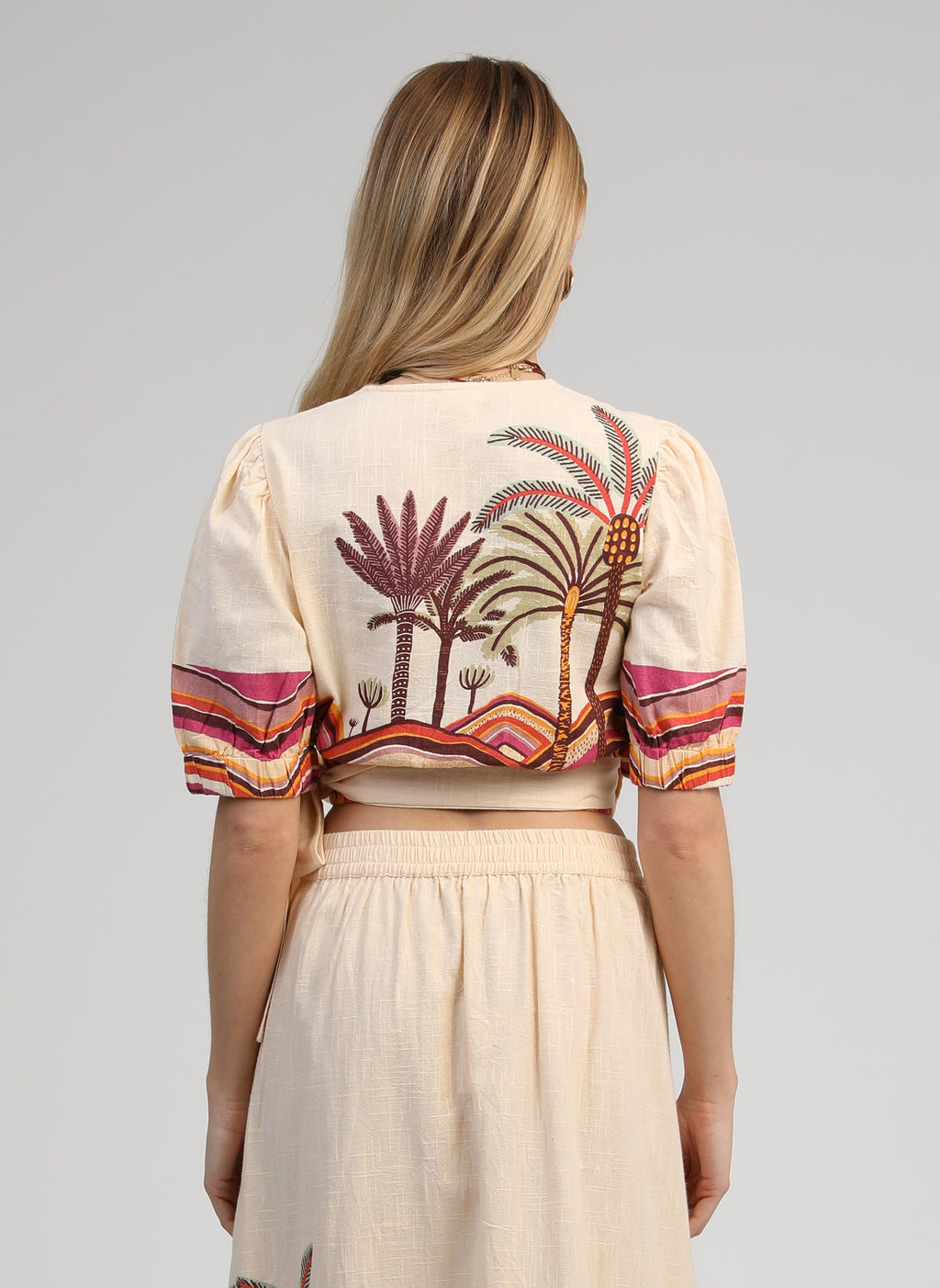 An'ge – Omlottopp Soriana Palmyre Rose, modell bakifrån i beige crop top med palmmönster och en långkjol