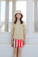Fille portant le BOB à imprimé fleurs jaunes, la chemise SASHA à manches longues imprimé fleurs jaunes et le short KIM à rayures rouges, en coton bio style vintage mixte et unisexe