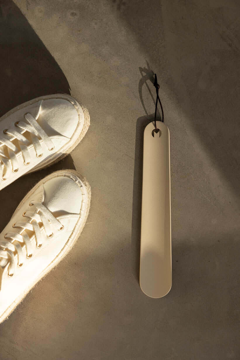 Schuhlöffel TILO in minimalist Gestaltung neben white Sneakern auf grauem Undertergrund.
