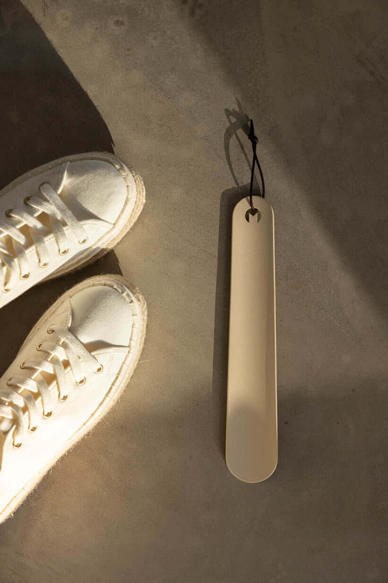 Schuhlöffel TILO in minimalist Gestaltung neben white Sneakern auf grauem Undertergrund.