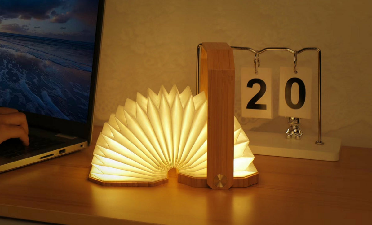 Gingko Design – Lampa Smart Origami - Naturalny Bambus, świecąca lampa w kształcie otwartej książki leżąca na biurku obok komputera
