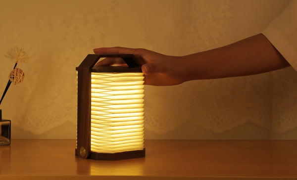 Gingko Design – Lámpara Smart Origami, lámpara plegable de madera y papel, colocada sobre una mesa de madera