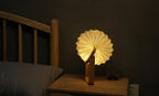 Gingko Design – Lampa Smart Origami - Naturalny Bambus, składana lampka nocna z drewna i papieru, włączona, na stoliku nocnym