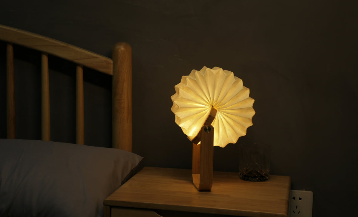 Gingko Design – Lampa Smart Origami - Naturalny Bambus, składana lampka nocna z drewna i papieru, włączona, na stoliku nocnym