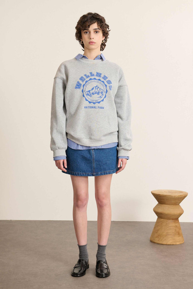 Mannequin femme de face portant un sweat ample coloris gris, col rond, manches longues et imprimé sur le devant.