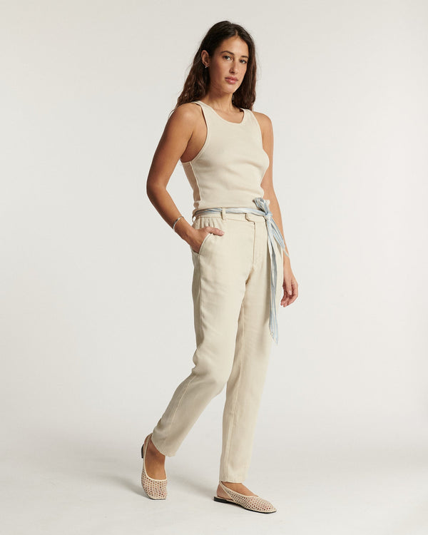 Women's jeans in light foam-colored canvas, fitted straight cut with thin knotted belt, offering elegant and easy-to-wear summer comfort.