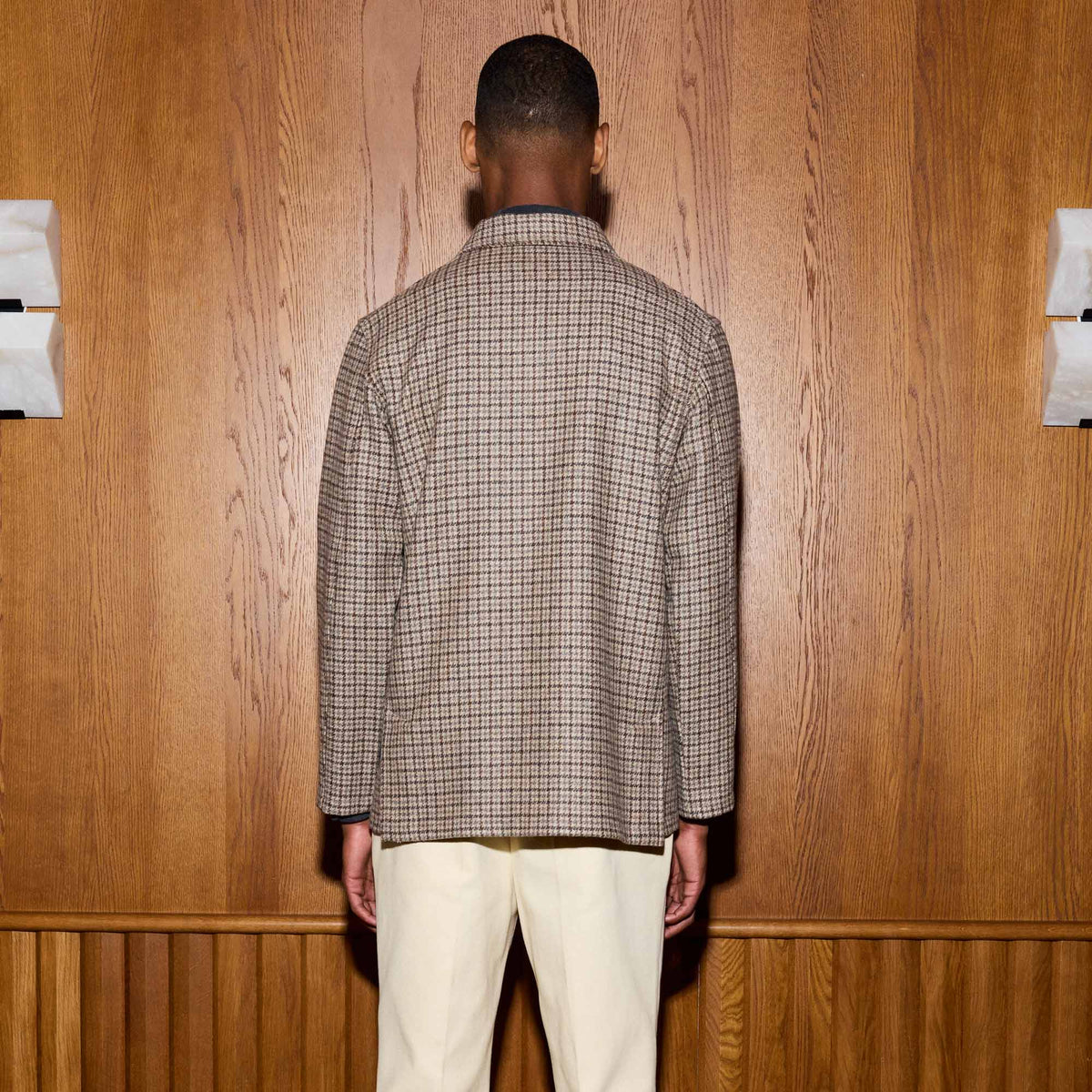 Hast – Brown Houndstooth Wool Overshirt, brown checked jacket seen from behind worn by a man, light trousers, wooden background