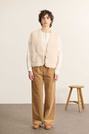 Mannequin de face portant une veste sans manches écru effet peau de mouton, coupe droite avec col rond et poches plaquées.