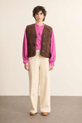 Modelo femenino de vista frontal con chaqueta sin mangas efecto borreguito marrón, corte recto con cuello alto.