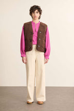 Modelo femenino de vista frontal con chaqueta sin mangas efecto borreguito marrón, corte recto con cuello alto.