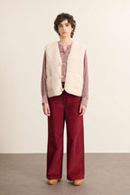 Fabriquée entièrement en polyester, veste sans manches POLETTE coloris écru avec bouton brandebourg.