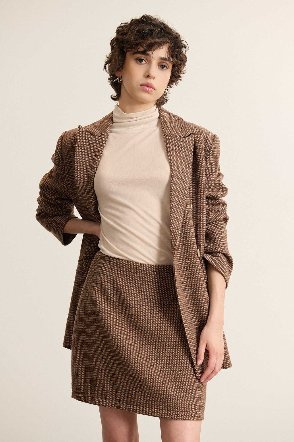 Jupe fabriquée en laine et polyester avec un tissu esprit pied de poule de couleur marron avec zip au dos. 