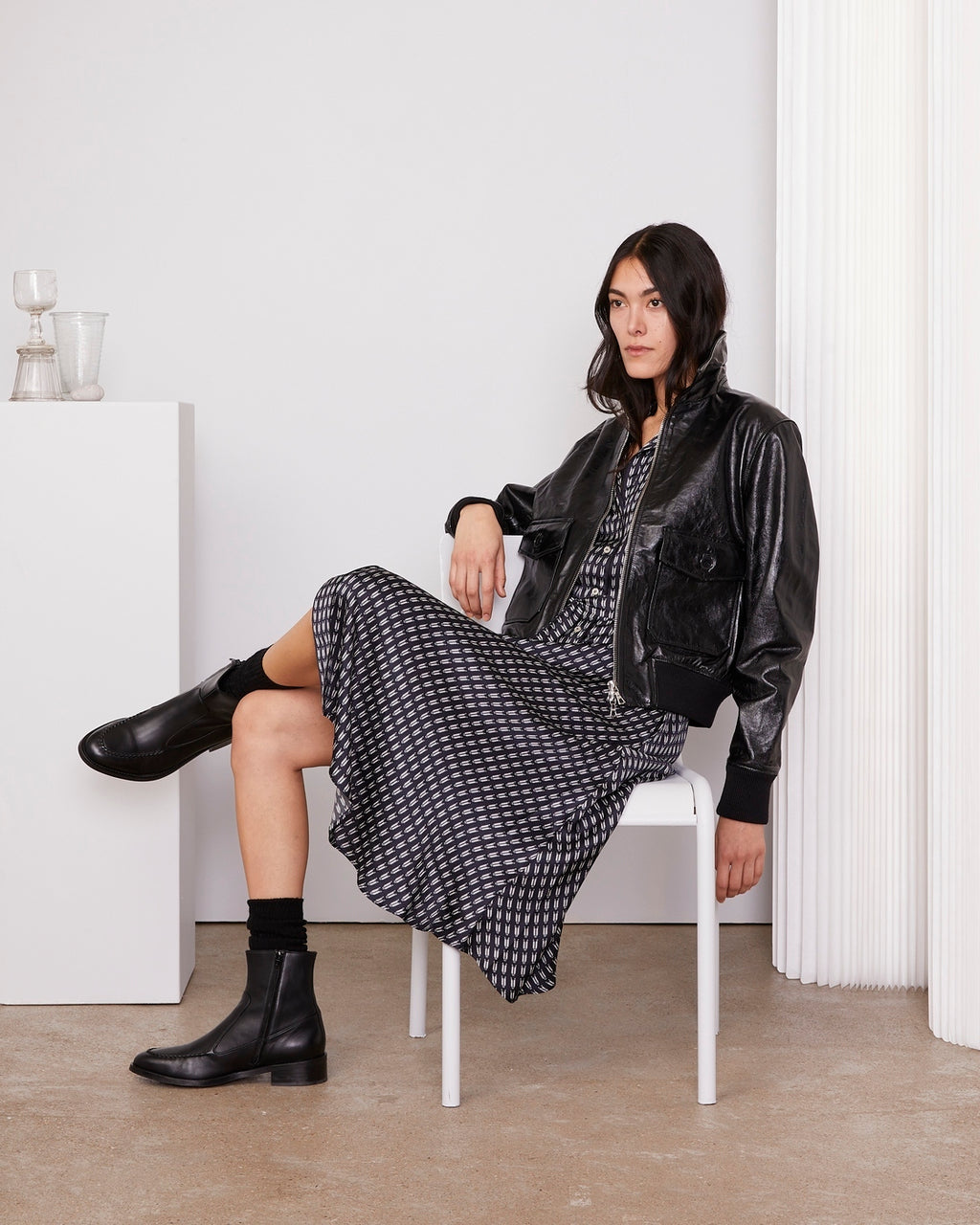 Officine Générale – Robe Benedicte - Bleu Marine/Écru - Femme, mannequin assise de profil, robe imprimée et blouson noir en cuir