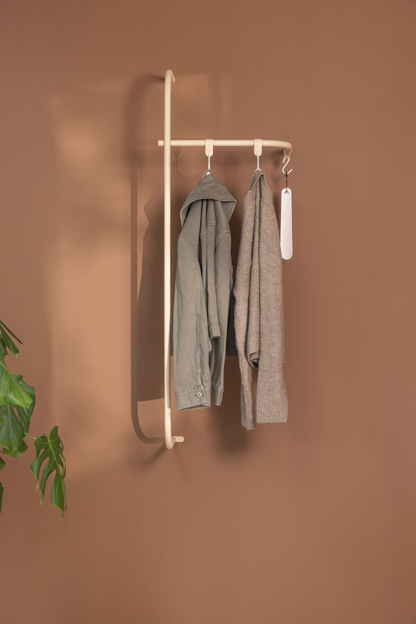 Wardrobe TAMINA with minimalist metal materials and hanging Kleidungsstücken an einer brown Wand.