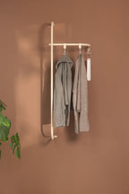 Wardrobe TAMINA with minimalist metal materials and hanging Kleidungsstücken an einer brown Wand.