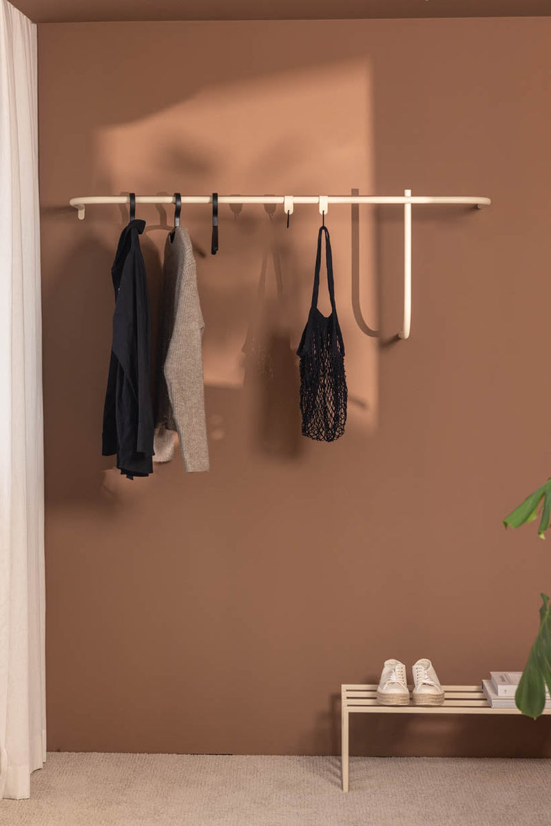 Armario TAMINA con materiales metálicos minimalistas y ropa en la pared, diseño elegante en colores cálidos.