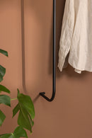 Armario TAMINA con Metallstangen minimalista y aufgehängtem Kleidungsstück an einer wandfarbenen Wand.