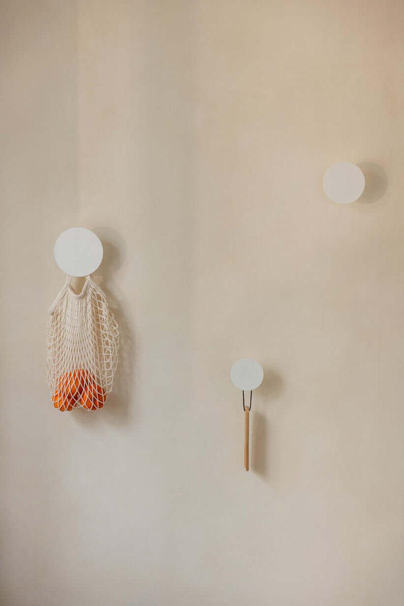 WANDHAKEN LOU (3er Set) an einer Wand mit Orangen in einer Netztasche und minimalistischen weißen Haken.