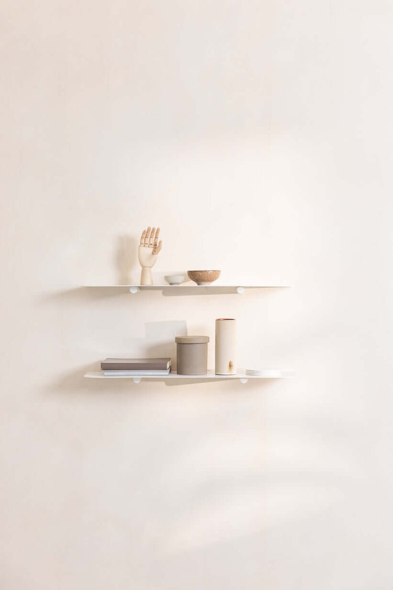 WANDREGAL LENN mit minimalistischen Regalen, dekoriert mit einer Hand, Schalen und Büchern an einer Wand.