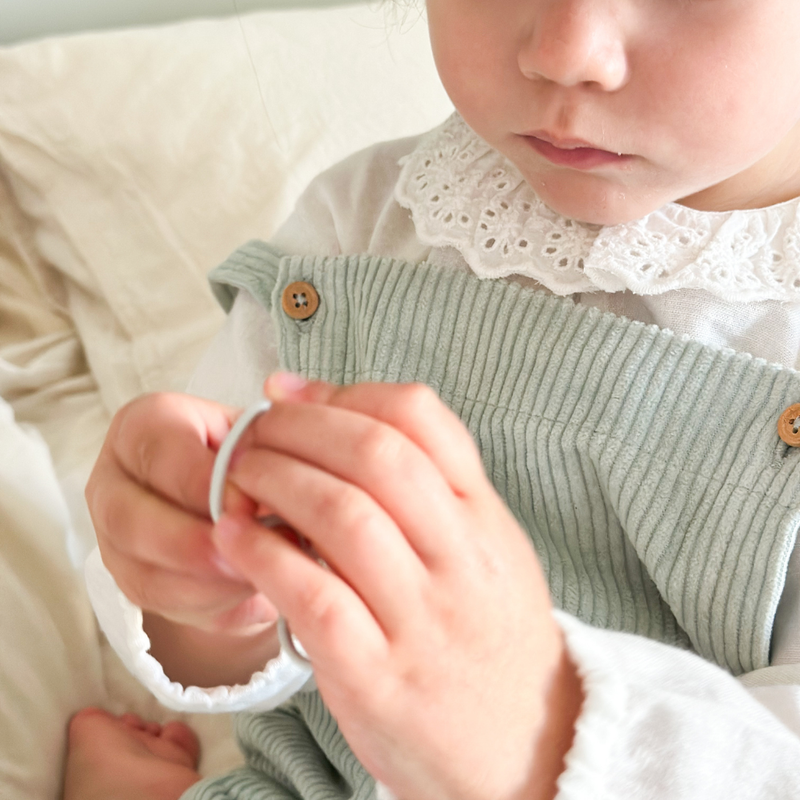 Zoom sur un élastique à cheveux fins de la marque Bachca dans les mains d'une petite fille.