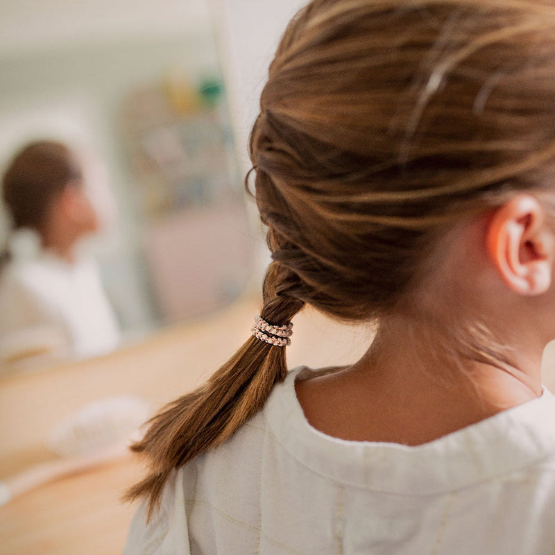 Petite fille portant une tresse attachée avec des élastiques fins pastel Bachca, accessoires cheveux doux et résistants, parfaits pour les coiffures d’enfants et les queues de cheval.