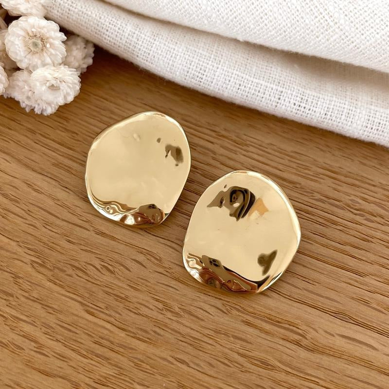 Instants Plaisirs – Boucles D'Oreilles Monica, deux boucles d'oreilles dorées, de forme irrégulière, sur une surface en bois