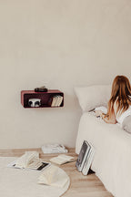 Hängender Nachttisch NELIO an einer Wand über einem Bett im Schlafzimmer mit Büchern und einem Kissen.