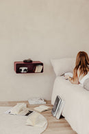 Hängender Nachttisch NELIO an einer Wand über einem Bett im Schlafzimmer mit Büchern und einem Kissen.
