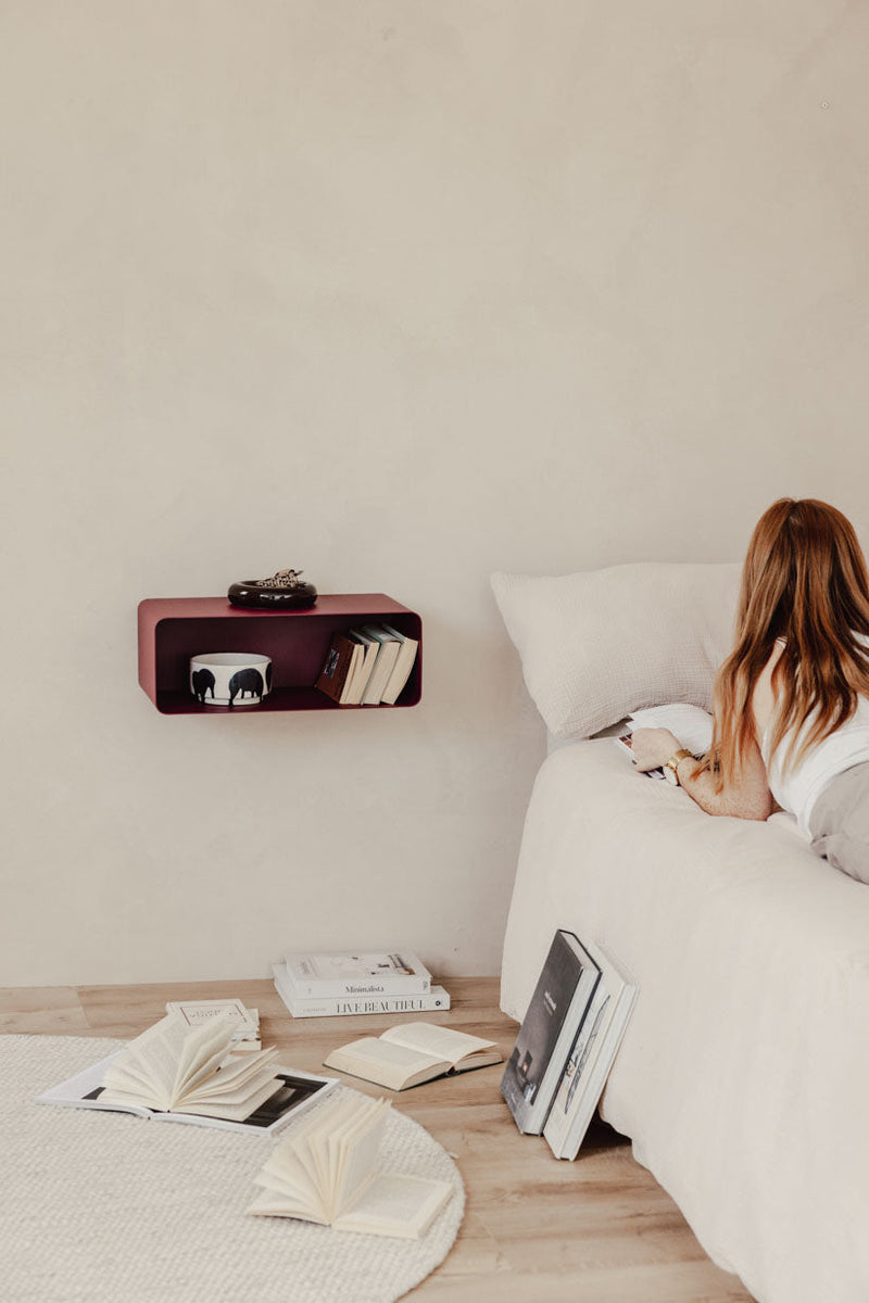 Hängender Nachttisch NELIO an einer Wand über einem Bett im Schlafzimmer mit Büchern und einem Kissen.