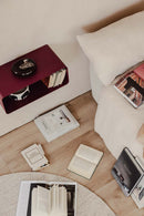 Hängender Nachttisch NELIO in modernm Design neben einem Sofa mit Bücherstapel auf dem Boden.