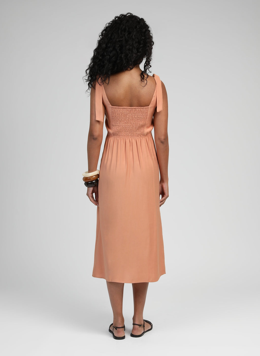 An'ge – Robe Midi Manta Terracotta, mannequin de dos portant une robe longue couleur pêche avec des sandales