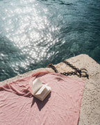 Open book on a blush pareo by the water with sunlight reflecting off the water.