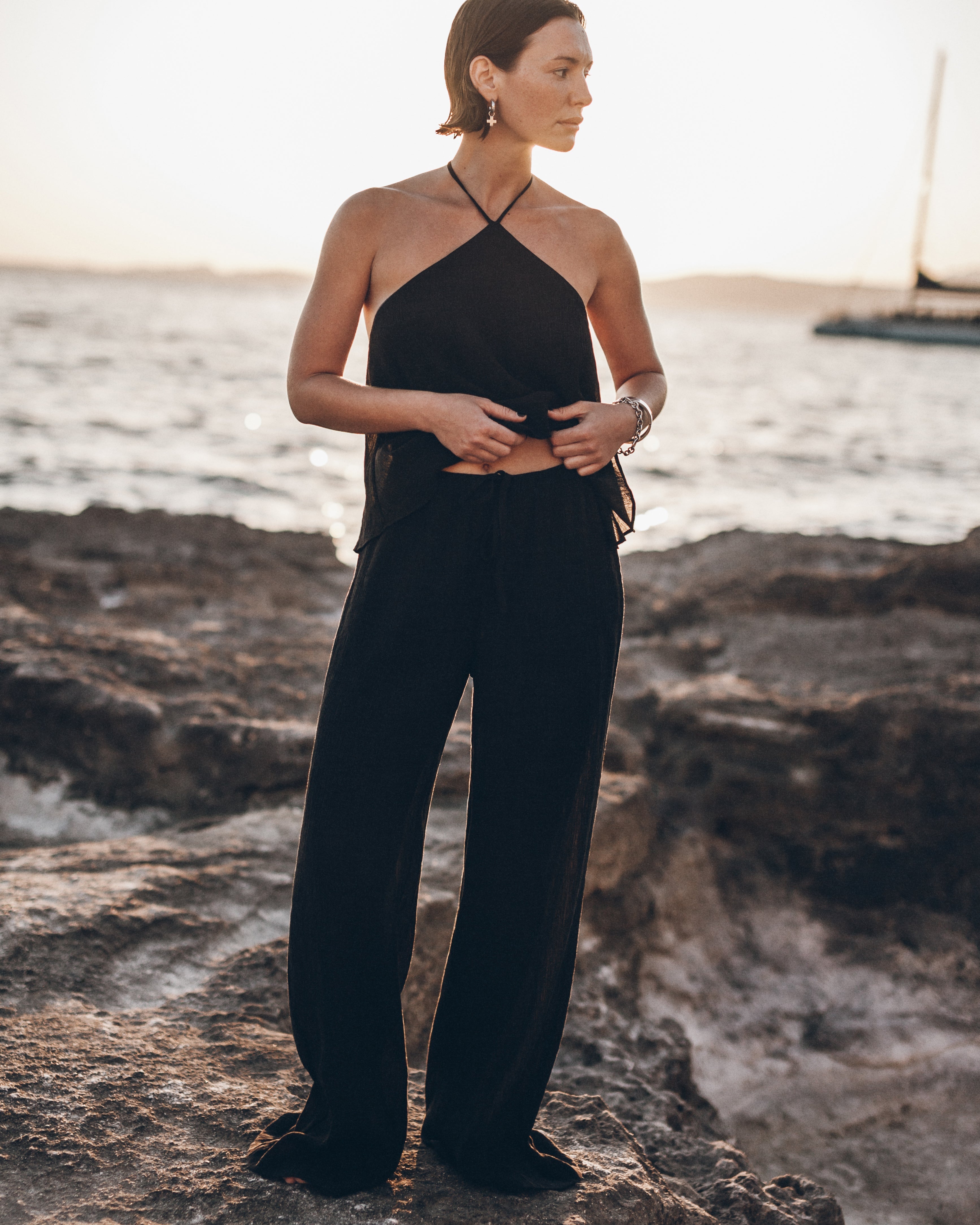 Woman in a black outfit standing on rocky terrain with water in the background