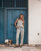 Woman wearing a striped tank top and jeans against a blue wall.