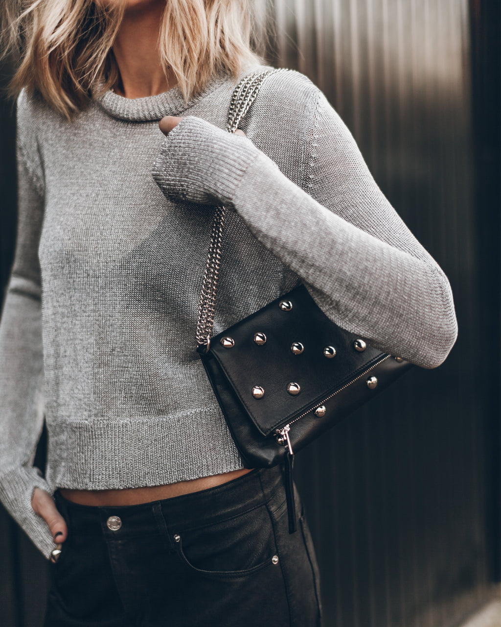 Person wearing a gray sweater holding a black studded handbag.