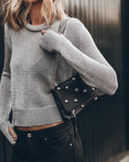 Person wearing a gray sweater holding a black studded handbag.