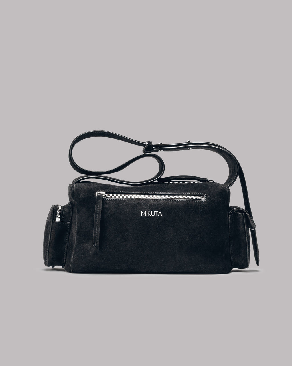 Dark suede handbag with a strap on a gray background