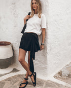 Woman in a white t-shirt and black skirt standing against a white wall.