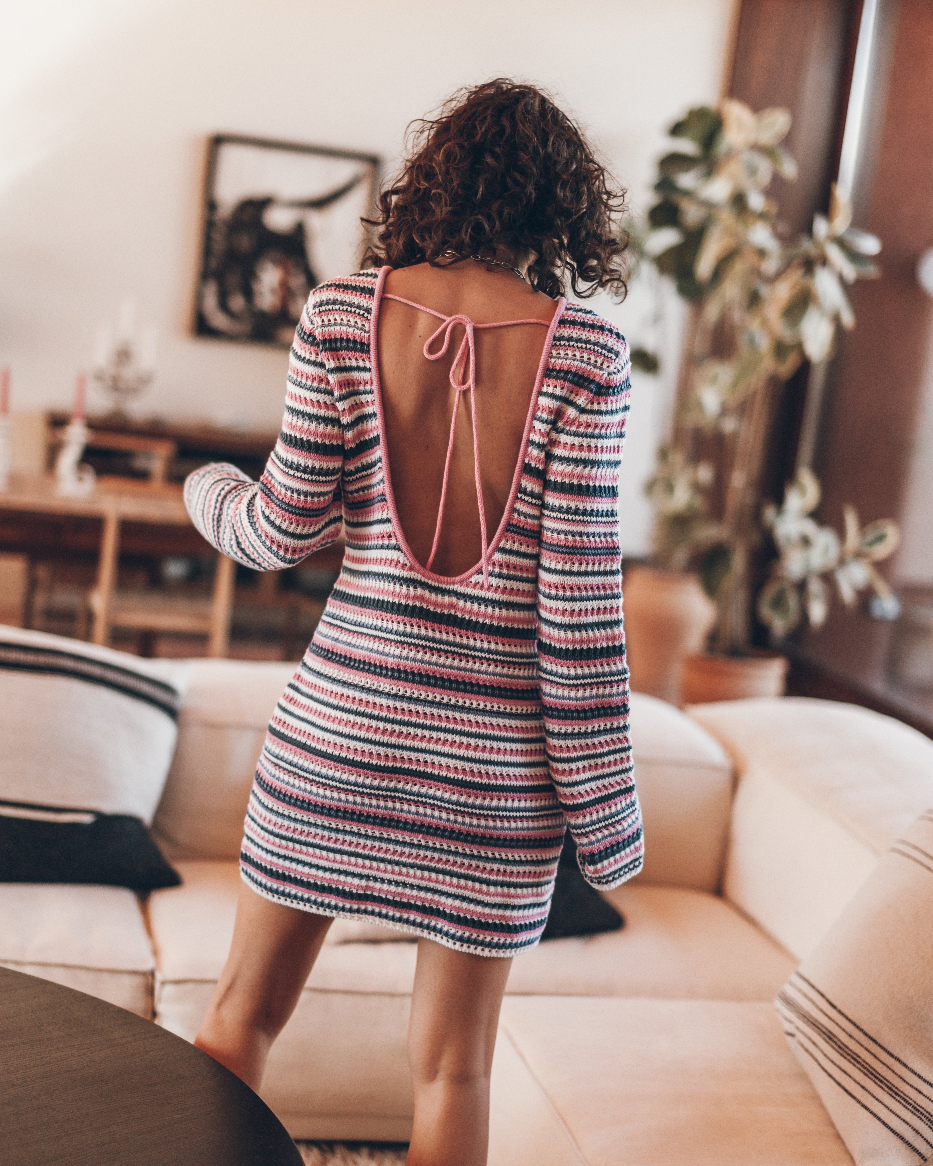 Woman wearing a striped dress with an open back in a living room.