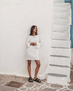 Woman in a white dress standing against a white wall.