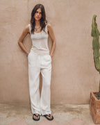 Woman in a white outfit standing against a beige wall with a cactus plant.