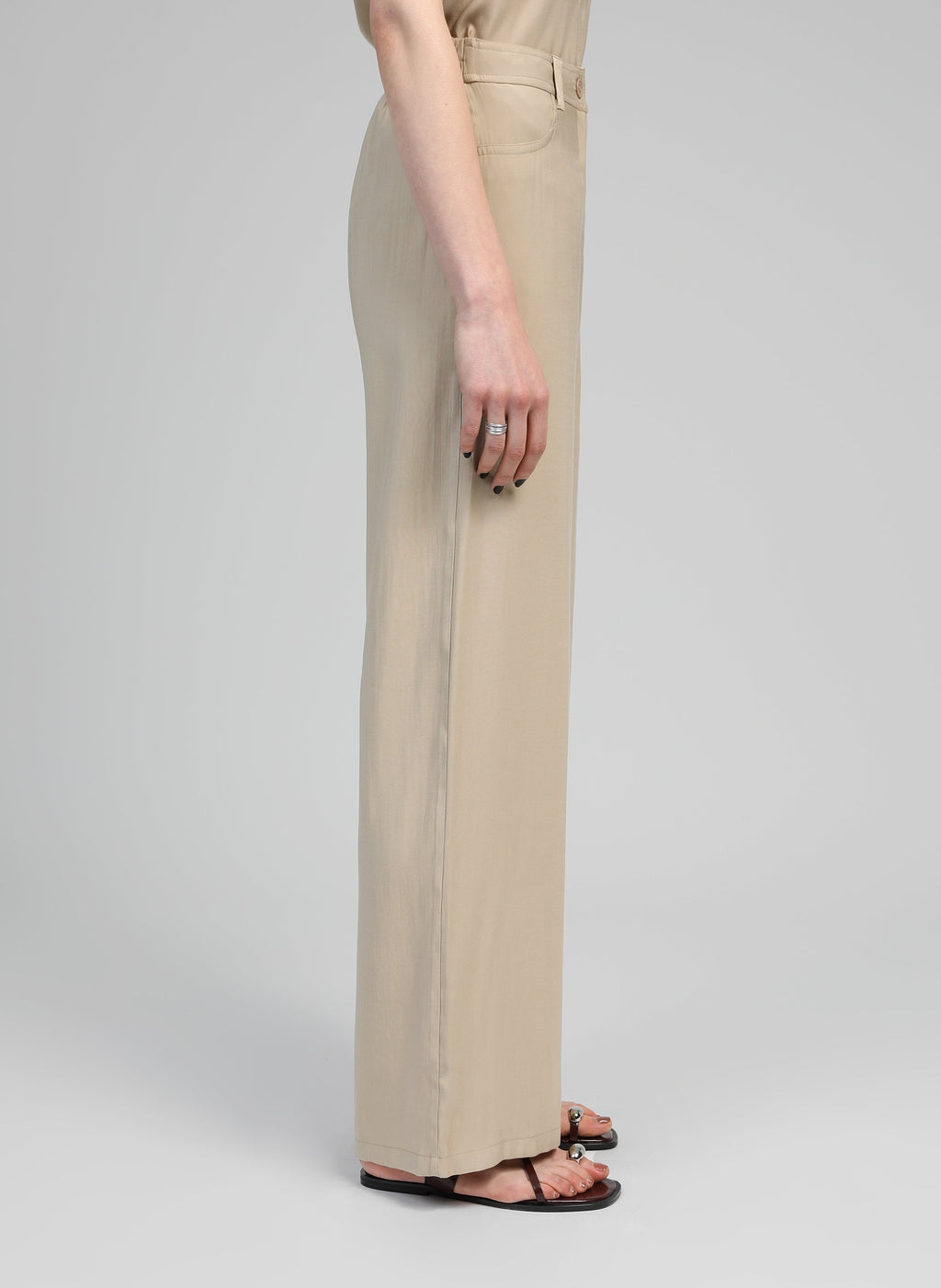 An'ge – Pantalon Phoebila Beige, pantalon beige porté par un mannequin, vue de profil, avec sandales