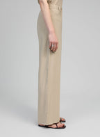 An'ge – Pantalon Phoebila Beige, pantalon beige porté par un mannequin, vue de profil, avec sandales
