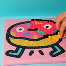 Main posant des pompons sur tableau Donut OMY – Développement de la motricité fine