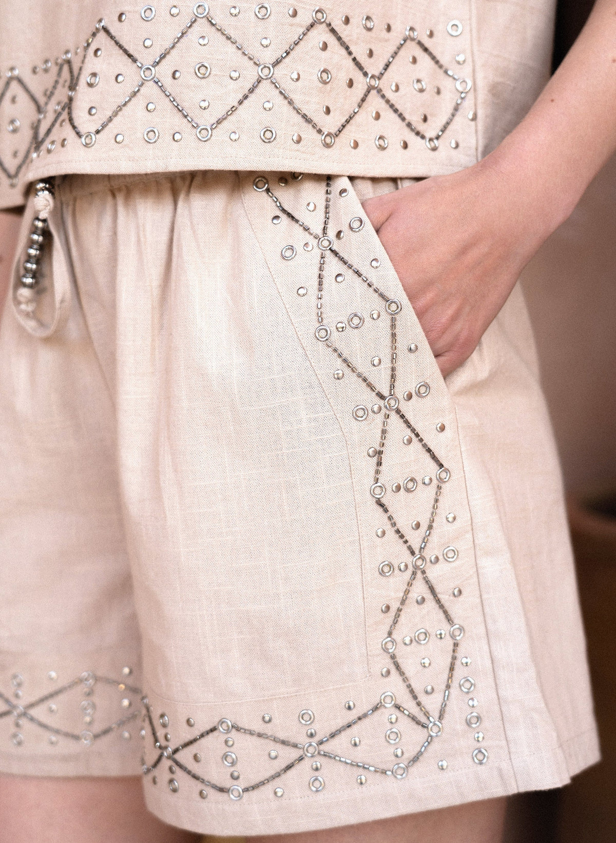 An'ge – Short Ramalo Lin, shorts beiges brodés de perles et de clous, portés par un mannequin