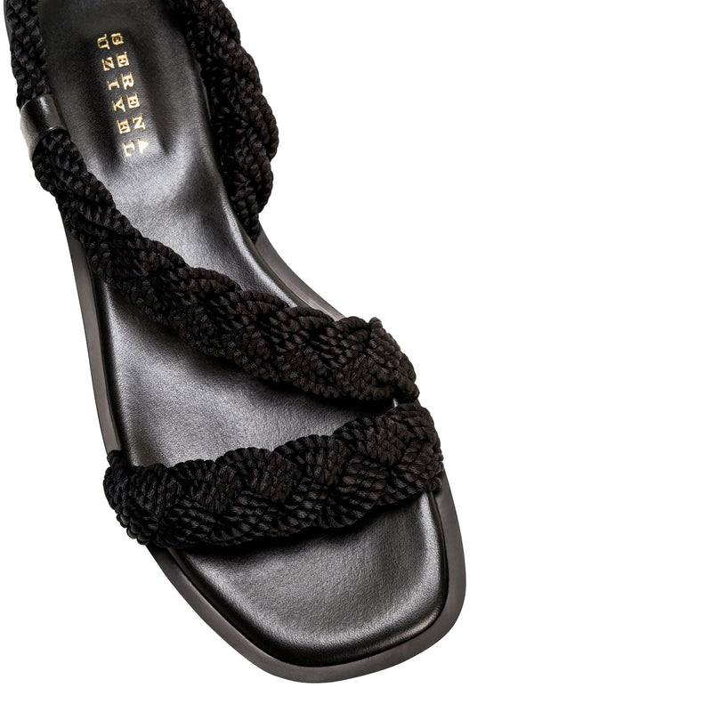 Ronda Black Flat Asymmetric Sandal featuring braided black straps and a sleek leather sole, perfect for summer wear.