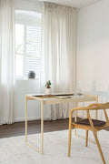 Skrivebord DONNA i et moderne rum med stol og planter på bordet, vindue med gardiner i baggrunden.