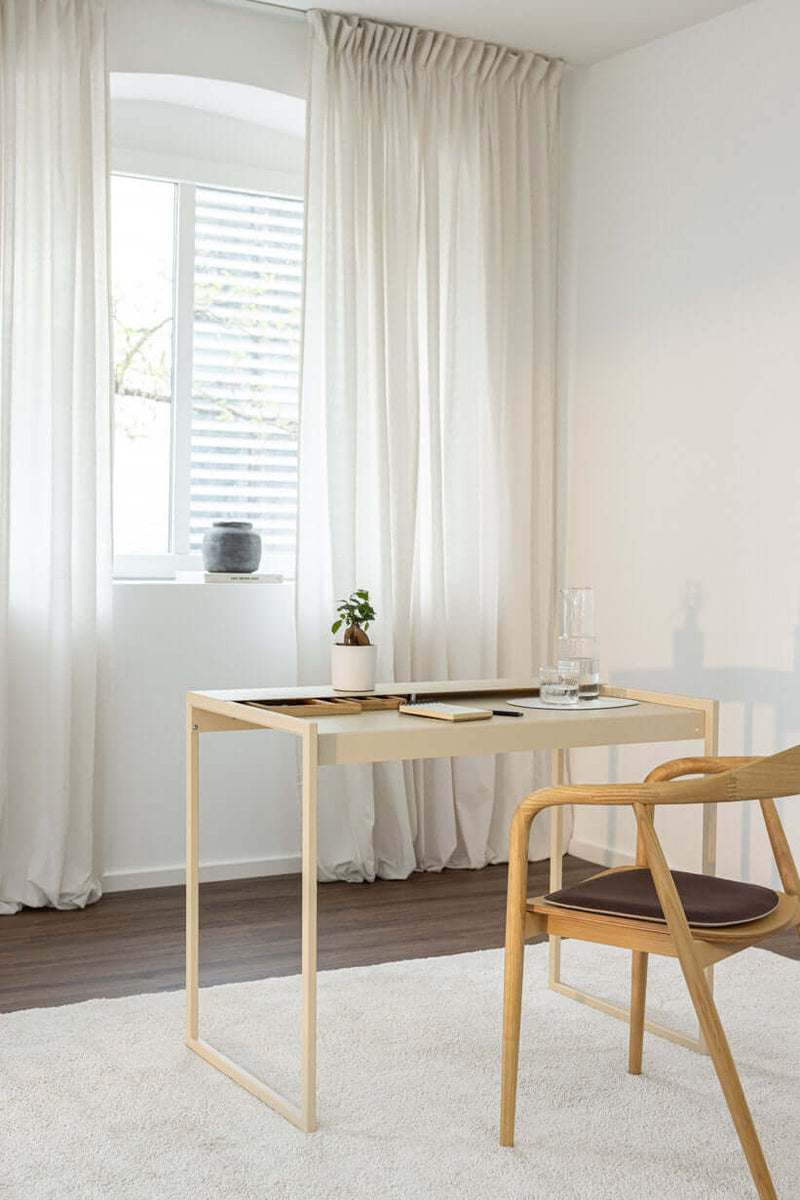 Schreibtisch DONNA in einem modernen Raum mit Stuhl und Pflanzen auf dem Tisch, Fenster mit Vorhängen im Hintergrund.