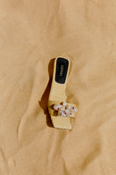 Taurea Natural Flat Sandal in sand colored raffia with stone embellishments on beach sand.