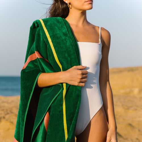 Mujer en traje de baño blanco sosteniendo una toalla de playa verde en la playa